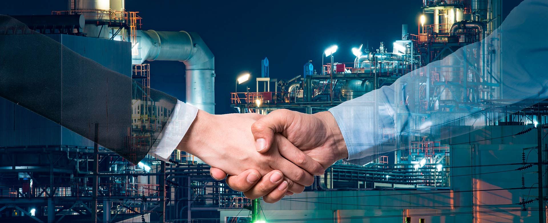 A handshake over an industrial site at night